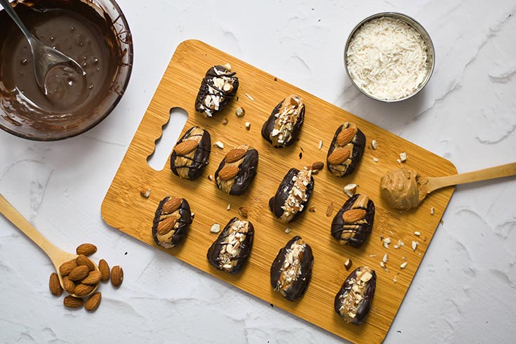 Adding an almond and topping to pitted dates sitting on a cutting board.