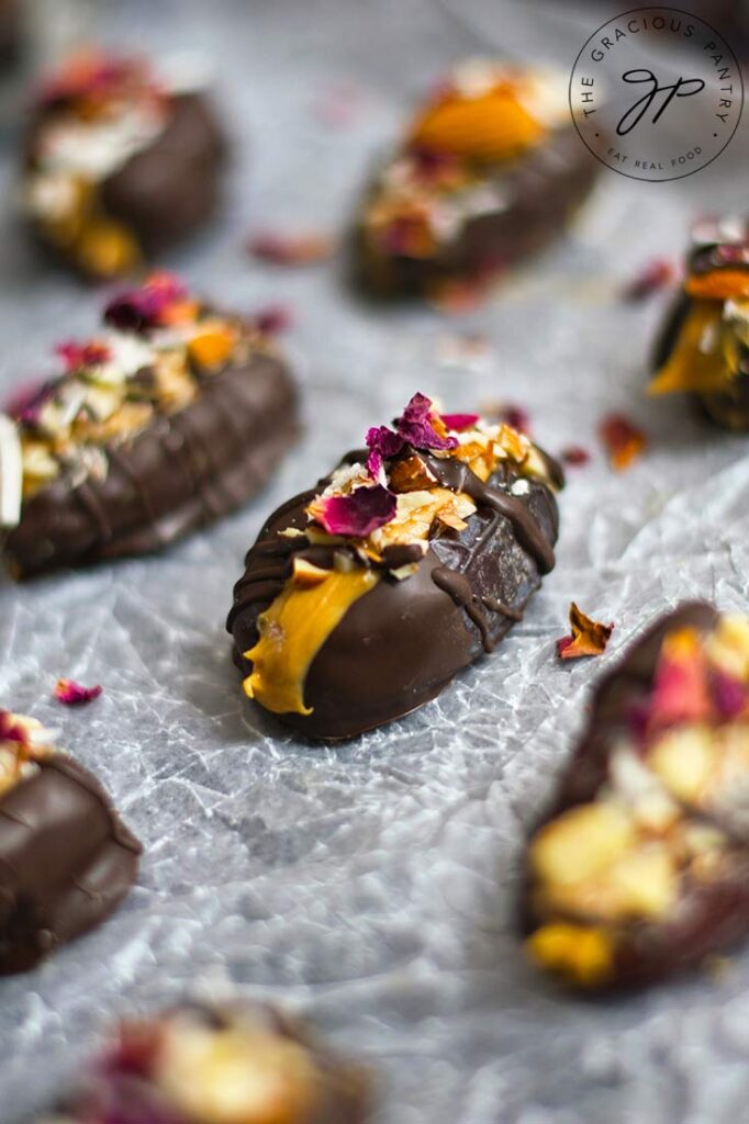 Garnished stuffed dates sit on a piece of parchment paper, lined up in rows.