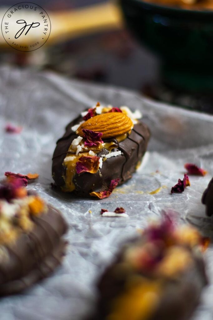 A single, stuffed date with an almond on top and sitting on parchment paper