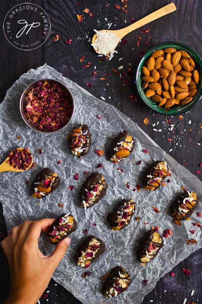 A female hand places a just-stuffed date onto a piece of parchment paper next to rows of other stuffed dates.