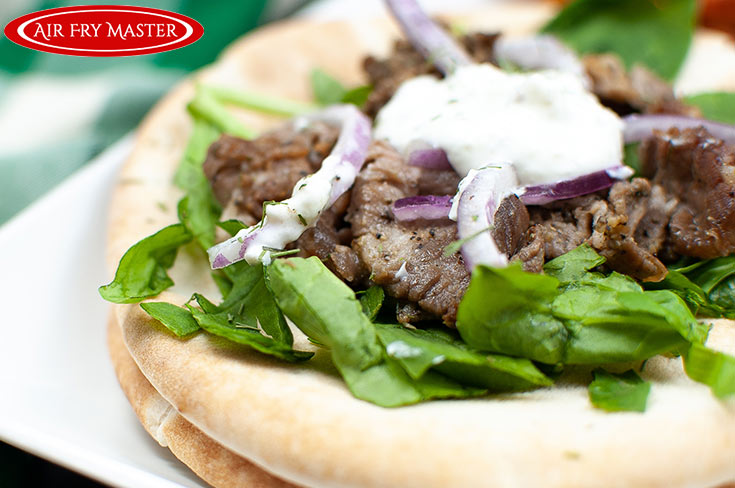 A steak gyro on a white plate, topped with yogurt sauce and red onion slices.