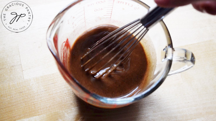 Almond Butter Fat Bombs Recipe ingredients being whisked together in a glass measuring cup.