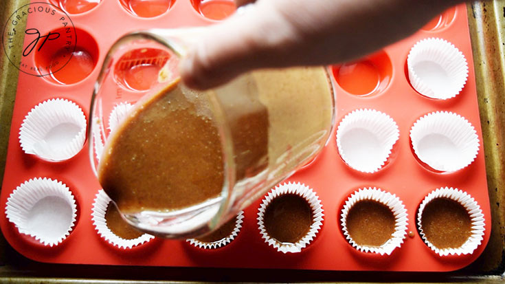 Pouring the almond butter bomb mixture into the paper mini muffin liners.