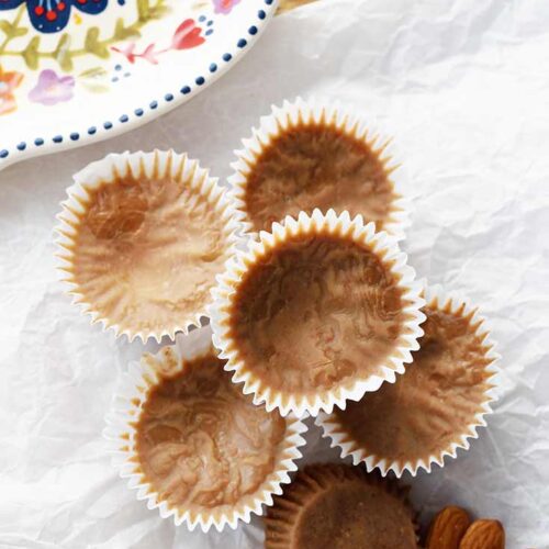 A stack of Almond Butter Fat Bombs sits on a piece of parchment paper which sits on a wooden cutting board.