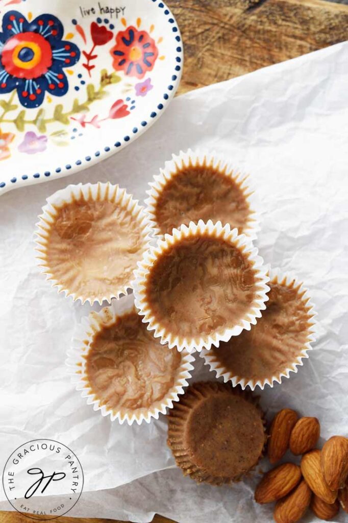 A stack of Almond Butter Fat Bombs sits on a piece of parchment paper which sits on a wooden cutting board.