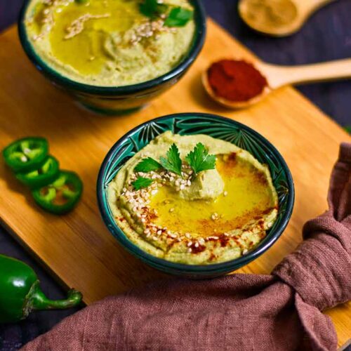 A side view of two lack and green bowls filled with Avocado Hummus.