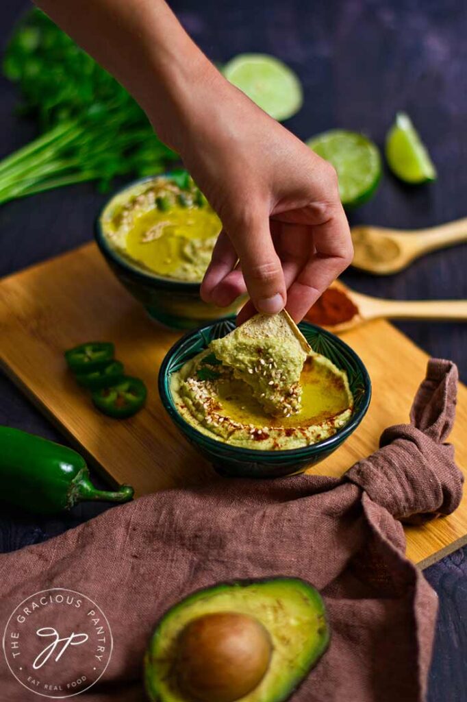 A woman's hand dipping a cracker into a bowl of avocado hummus.