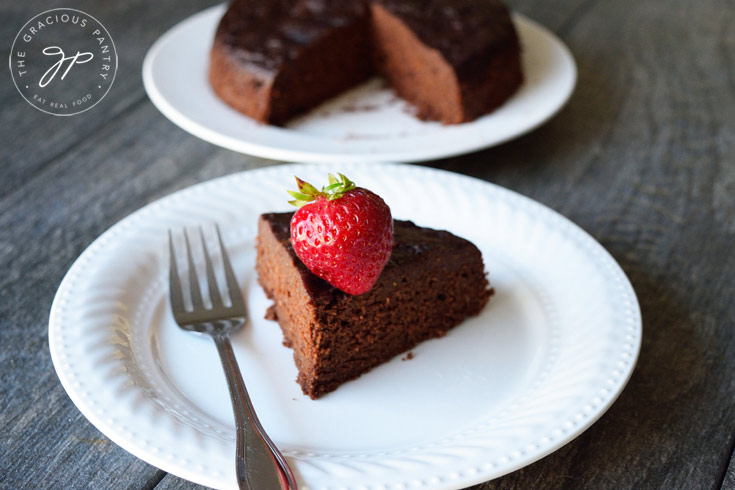A slice of Instant Pot Chocolate Cake sits on a white plate with a fork resting at it's side.
