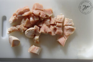 Chicken cut into stew-sized pieces, sitting on a white cutting board.