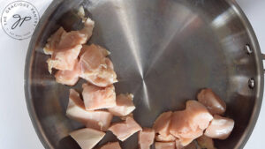 Cut chicken sitting in a stainless steel skillet.