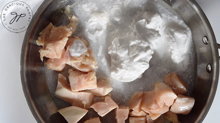 Coconut milk added to chicken pieces in a skillet.