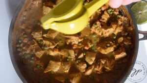 Sprinkling fresh lime juice over the finished Coconut Curry Chicken in a skillet.