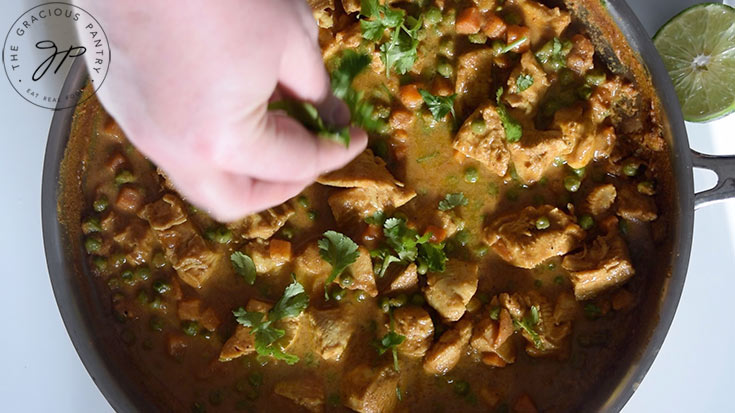 Garnishing the Coconut Curry Chicken Recipe with fresh cilantro in the same skillet it was cooked in.