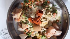 Seasonings and Thai curry paste added to a skillet of veggies, chicken and coconut milk.