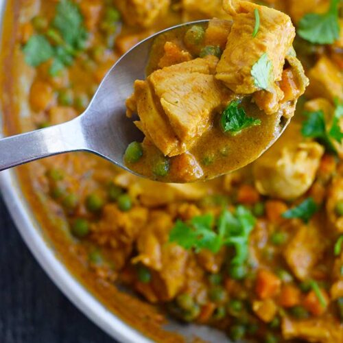 An overhead shot looking down on a serving spoon lifting some Coconut Curry Chicken towards the camera.