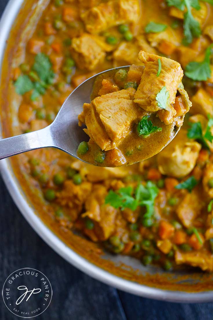 An overhead shot looking down on a serving spoon lifting some Coconut Curry Chicken towards the camera.