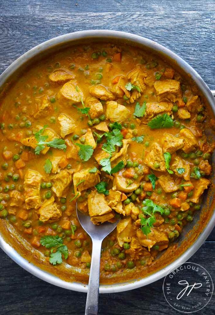 Coconut Curry Chicken, just cooked, sitting in a skillet. A serving spoon rests in the skillet.