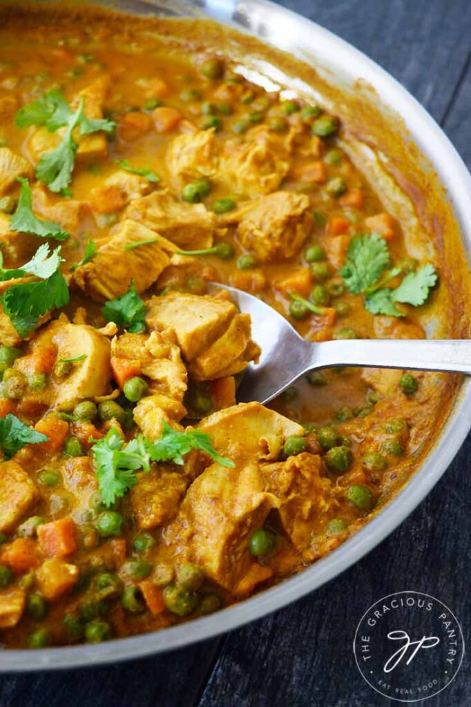 A close up of a serving spoon resting in a skillet filled with Coconut Curry Chicken.