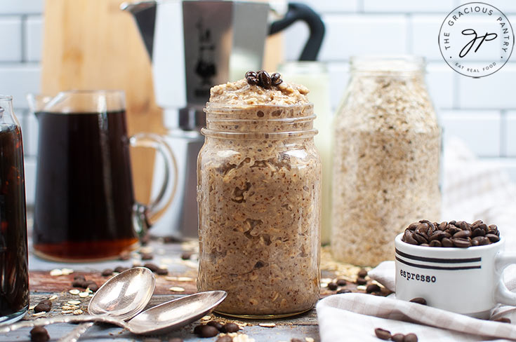 The finished Coffee Overnight Oats sitting on a wooden table next to a pitcher of coffee and a jar of dry oats.