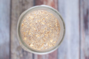All the ingredients in this Coffee Overnight Oats Recipe combined in a canning jar which sits on a wooden table.
