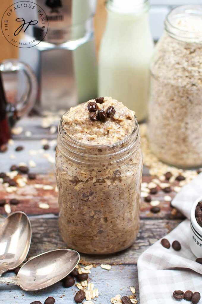 A side view of a canning jar filled with oatmeal. Coffee beans lay strewn over the table top.