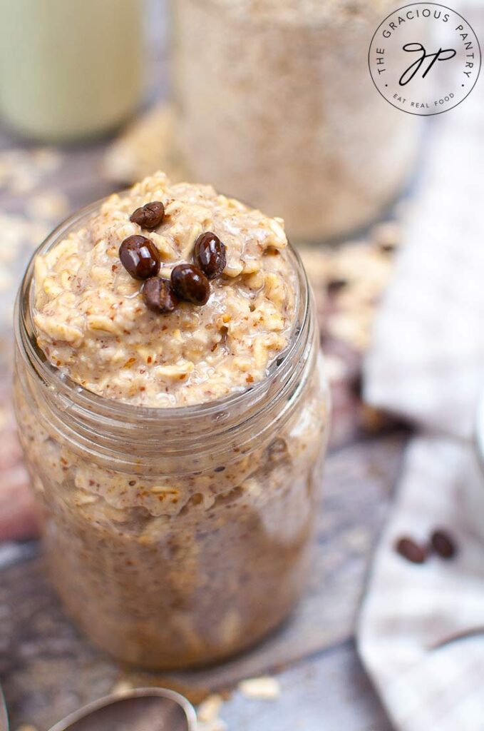 A canning jar on a wooden table sits filled with Coffee Overnight Oats and topped with a few coffee beans.