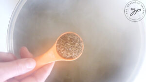 Caraway seed in an orange measuring spoon, about to be added to a stock pot of broth.