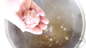 A rolled meatball about to be added to boiling broth.