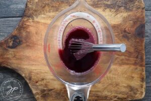 Grenadine Syrup, mixed and sitting in a measuring cup with a whisk resting inside the cup.