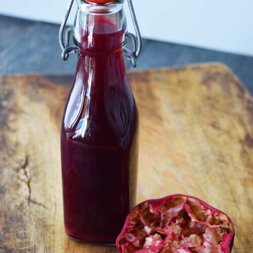 A capped, clear, glass bottle filled with Grenadine Syrup sits on a cutting board.