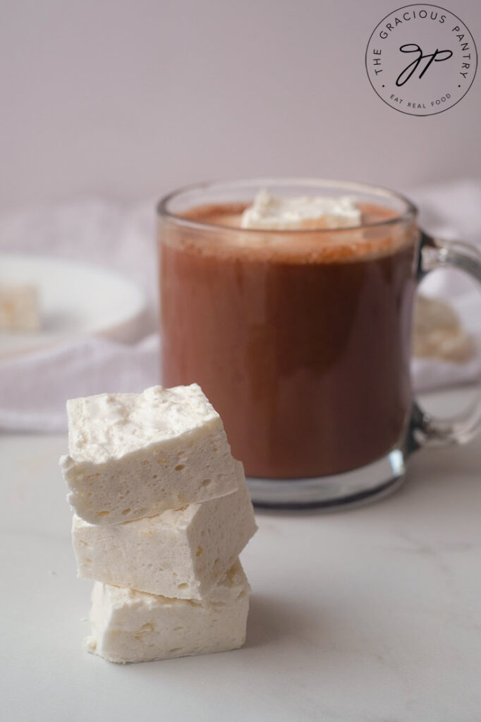 A stack of three marshmallows cut into squares, sitting in front of a mug of hot chocolate.