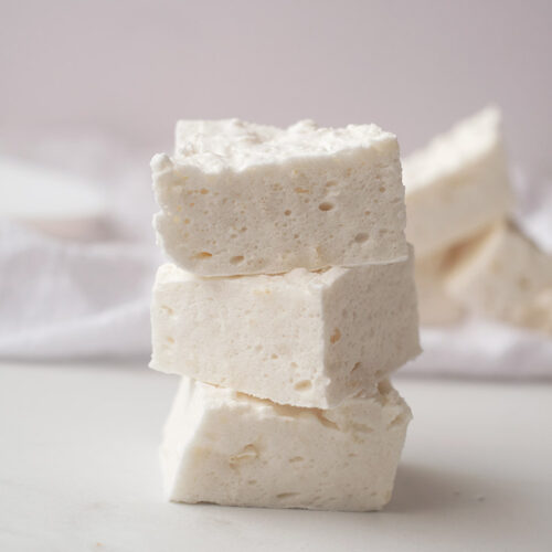 Three square marshmallows are stacked on a white, marble surface.