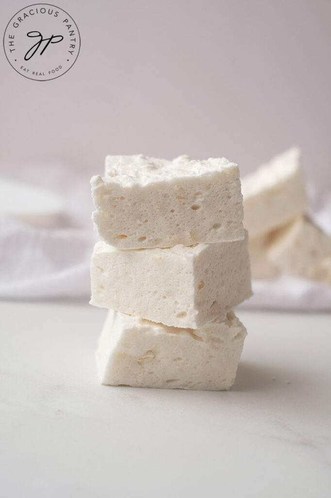 Three square marshmallows are stacked on a white, marble surface.