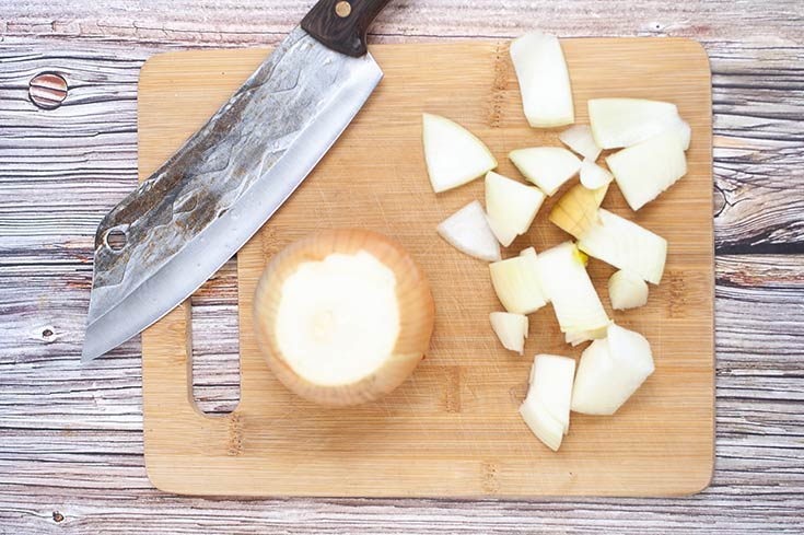 A knife and chopped onions rest on a wooden cutting board.