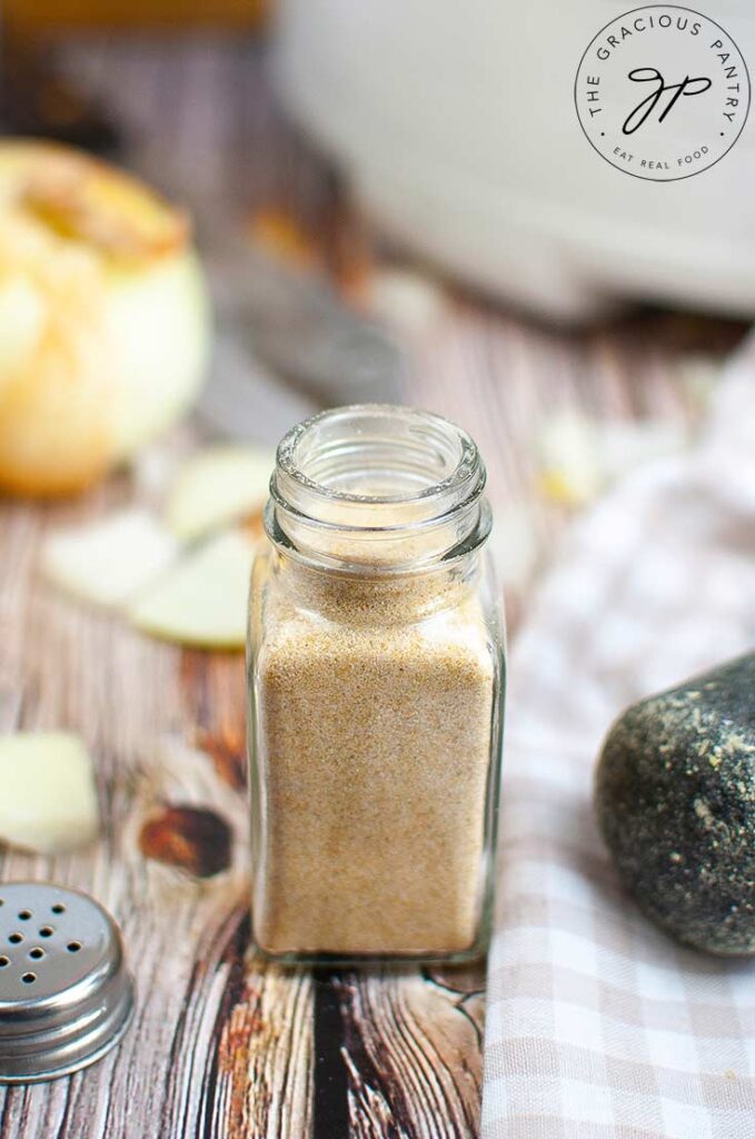 A side view of a spice bottle sitting on a table, filled with homemade onion powder. The jar lid sits to the left side of the jar.