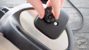 A hand closes the steam valve on an Instant Pot.