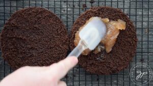 A spatula spreading fruit spread over one layer of a chocolate cake.