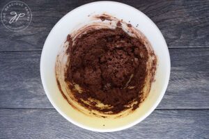 A thick, chocolate batter sits mixed in a white mixing bowl.