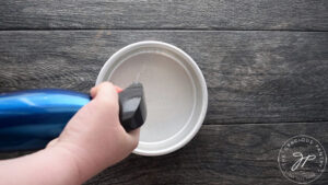 Spraying a 6-inch cake pan with an oil sprayer.