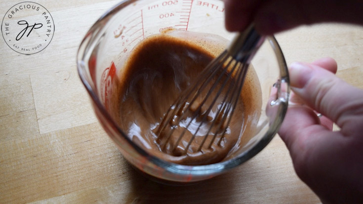 A whisk, whisking together ingredients in a glass measuring cup.