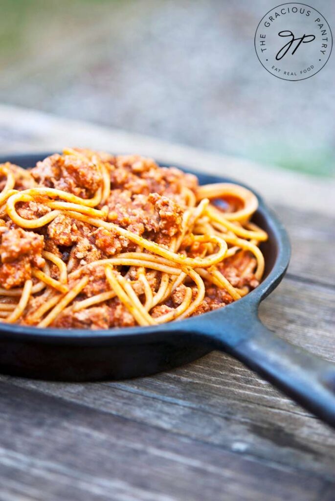 A side view of Skillet Spaghetti in a cast iron skillet, sitting on a wooden table.