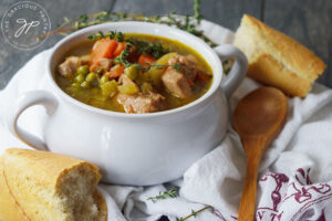 A white bowl filled with Slow Cooker Chicken Stew, surrounded by pieces of baguette and a wooden spoon.