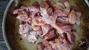 Raw, cut chicken thighs sitting in a skillet.