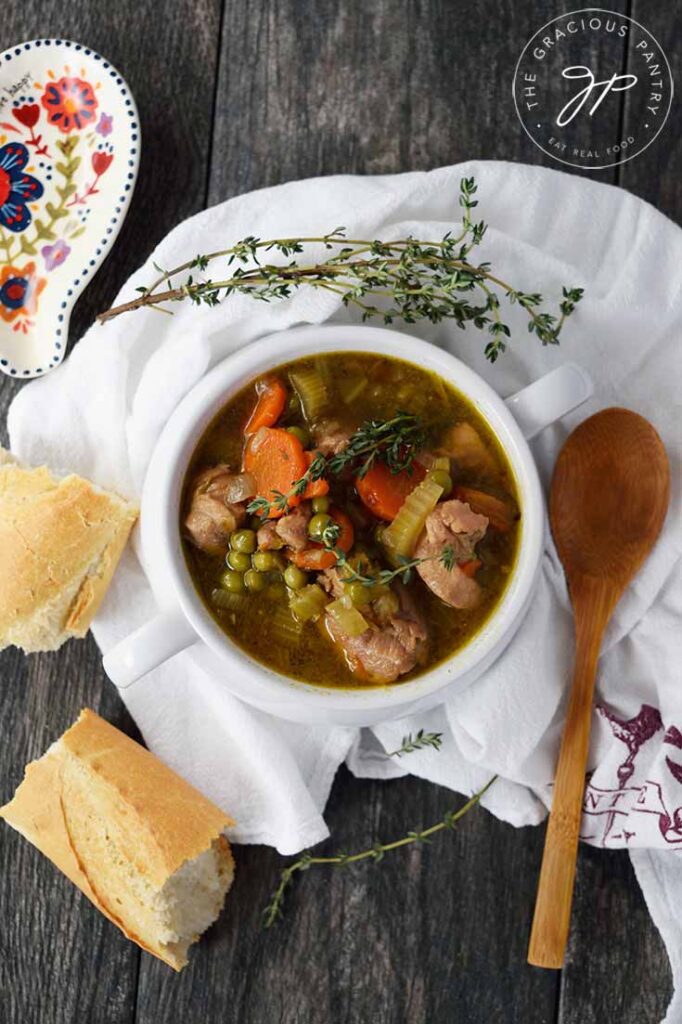 An overhead view looking down into a bowl filled with Slow Cooker Chicken Stew. A wooden spoon sits to the right of the bowl and pieces of baguette sit to the left.