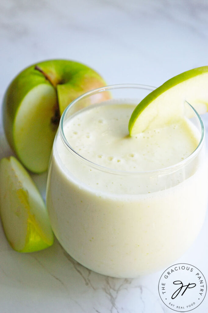 A Tart Green Apple Smoothie in a clear glass. A cut apple sits to the side of the glass.