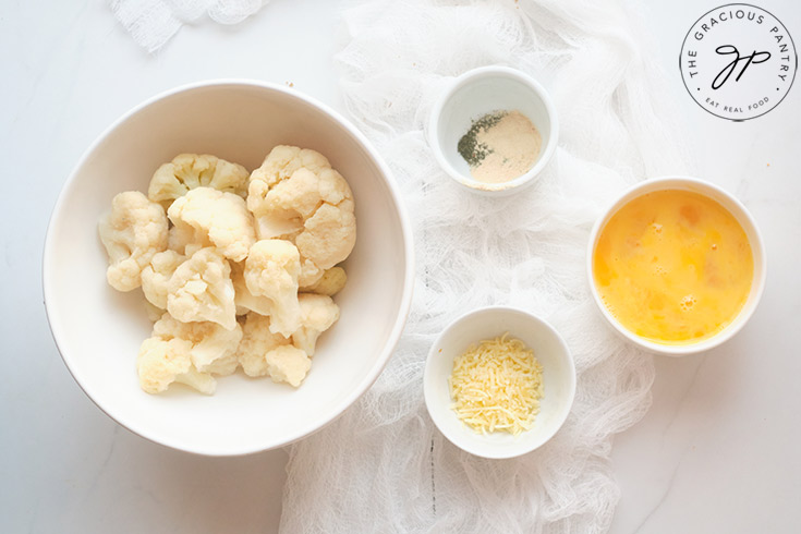 All the ingredients for this Cauliflower Fritters Recipe collected in small bowls and placed on a white surface.