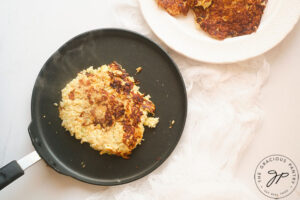 A single Cauliflower Fritter cooking on a hot, black skillet.