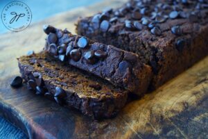 A partially sliced loaf of Chocolate Pumpkin Bread sitting on a cutting board.