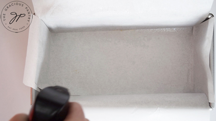 Spraying oil on a parchment lined loaf pan.