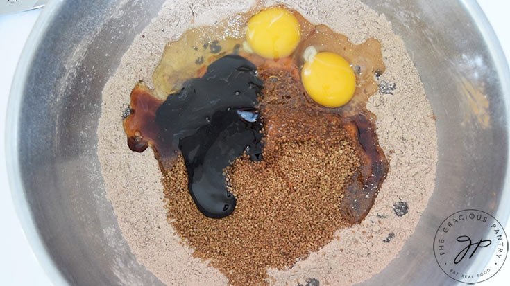 Eggs, molasses and vanilla extract sitting unmixed in a bed of flour mixture.